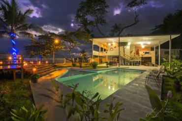 Casa Rio Mar villa lit up at dusk with its swimming pool, open-air terrace and tropical gardens under a purple sky in Jaco Beach, Costa Rica