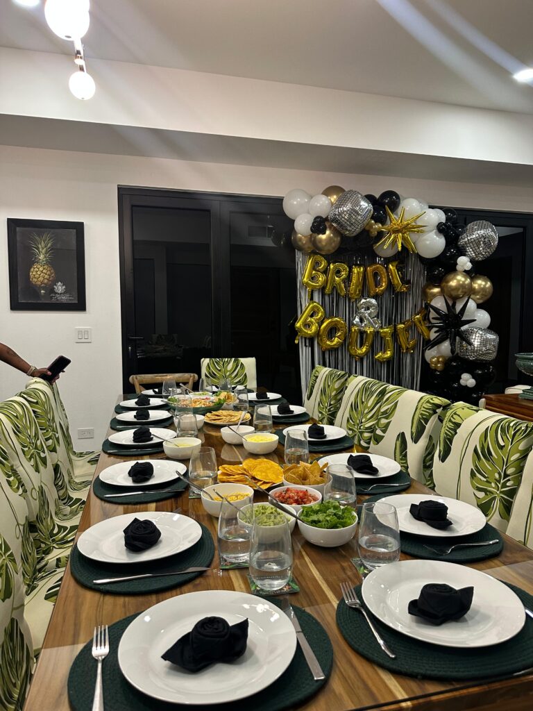 Bachelorette party dinner table set with black napkins and green placemats beside a gold "Bride & Boujee" balloon backdrop at Casa Rio Mar villa in Jaco Beach, Costa Rica