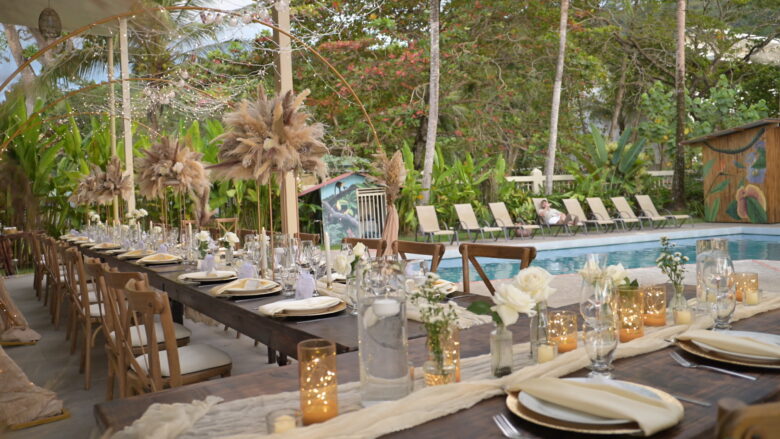 Long poolside wedding reception table set with pampas grass centrepieces, white roses and candles under fairy light arches at Casa Rio Mar in Jaco Beach, Costa Rica