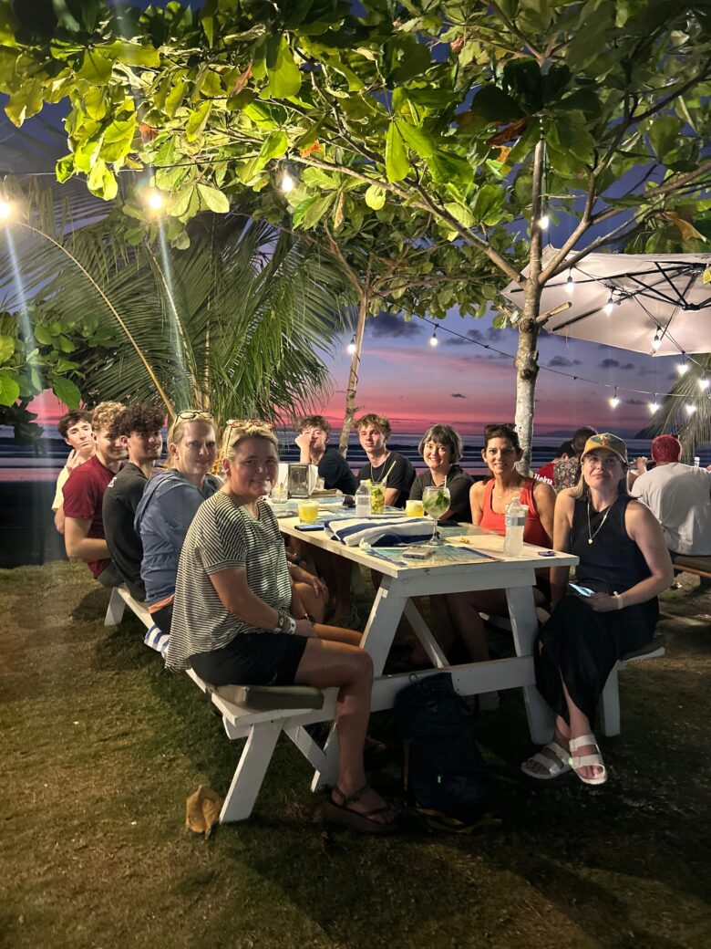 Wedding guests gathered at a beachfront picnic table under string lights and tropical trees at sunset in Jaco Beach, Costa Rica